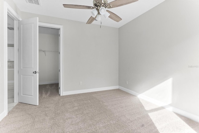 unfurnished bedroom featuring ceiling fan, light colored carpet, a walk in closet, and a closet