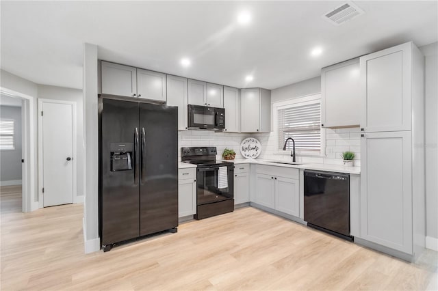 kitchen with black appliances, backsplash, light hardwood / wood-style floors, and sink