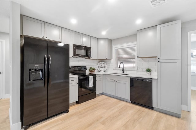 kitchen with black appliances, sink, gray cabinets, tasteful backsplash, and light hardwood / wood-style floors