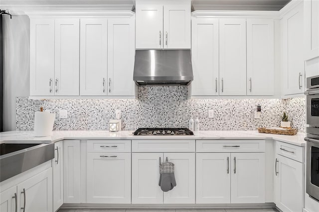 kitchen with wall chimney range hood, stainless steel gas cooktop, tasteful backsplash, light stone counters, and white cabinets