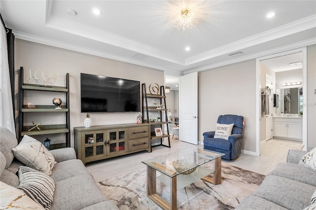 living room featuring a chandelier, light hardwood / wood-style floors, a raised ceiling, and crown molding