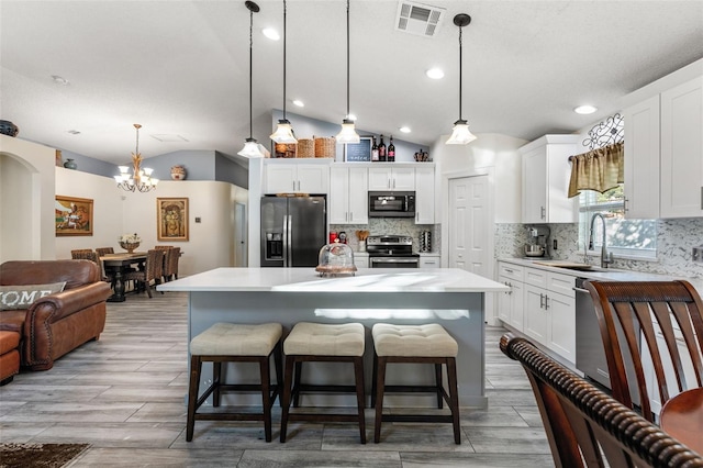 kitchen with white cabinets, hanging light fixtures, vaulted ceiling, a kitchen island, and stainless steel appliances