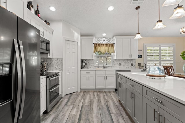 kitchen with pendant lighting, sink, gray cabinets, white cabinetry, and stainless steel appliances