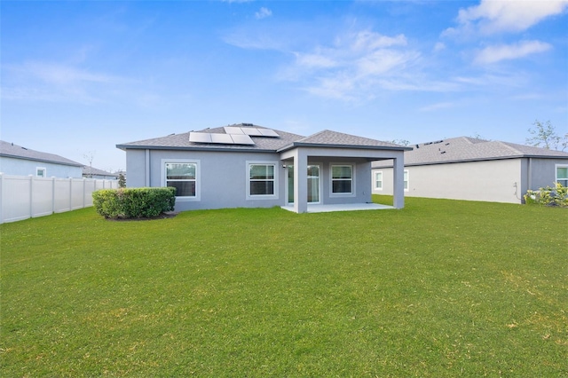 rear view of property featuring solar panels, a patio, and a lawn