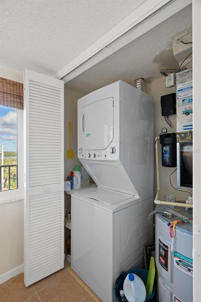 laundry area featuring light tile patterned floors, a textured ceiling, electric water heater, and stacked washer and clothes dryer