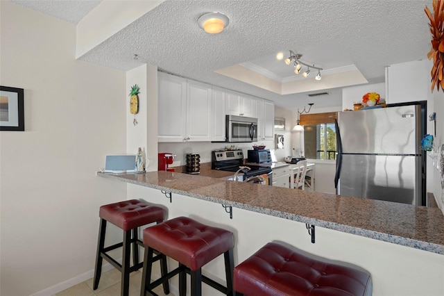 kitchen featuring white cabinetry, a kitchen breakfast bar, kitchen peninsula, a tray ceiling, and appliances with stainless steel finishes