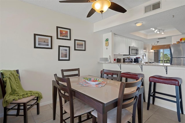 dining area with a tray ceiling, light tile patterned floors, and a textured ceiling