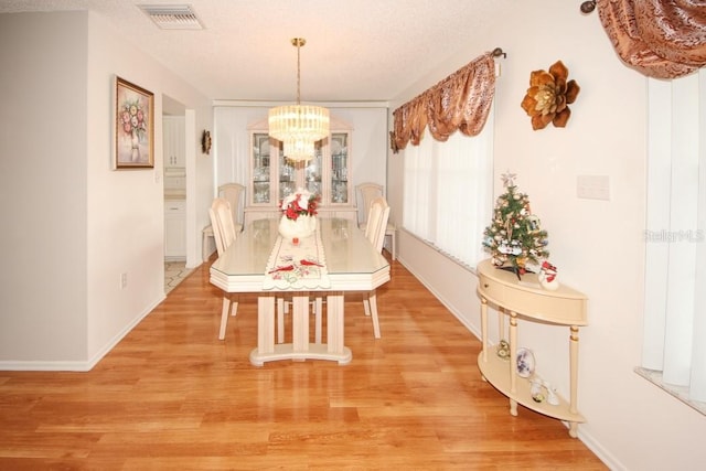 dining space featuring a chandelier, light wood finished floors, visible vents, and baseboards