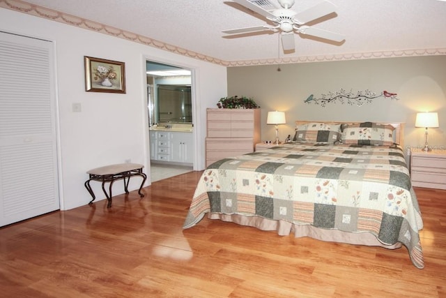 bedroom with a textured ceiling, ceiling fan, wood finished floors, visible vents, and ensuite bath