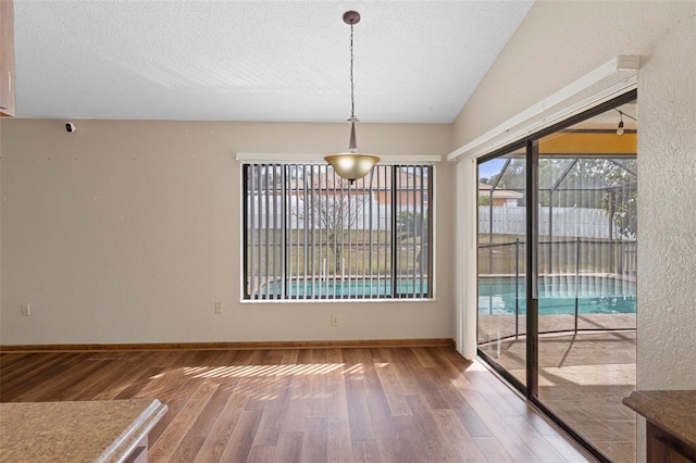 unfurnished dining area with hardwood / wood-style floors, lofted ceiling, and a textured ceiling