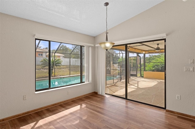 unfurnished dining area with wood-type flooring, a textured ceiling, vaulted ceiling, and ceiling fan