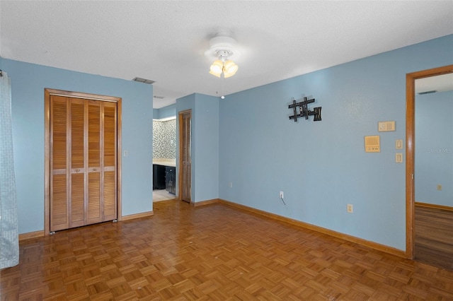 unfurnished bedroom with ensuite bathroom, ceiling fan, a textured ceiling, and parquet flooring