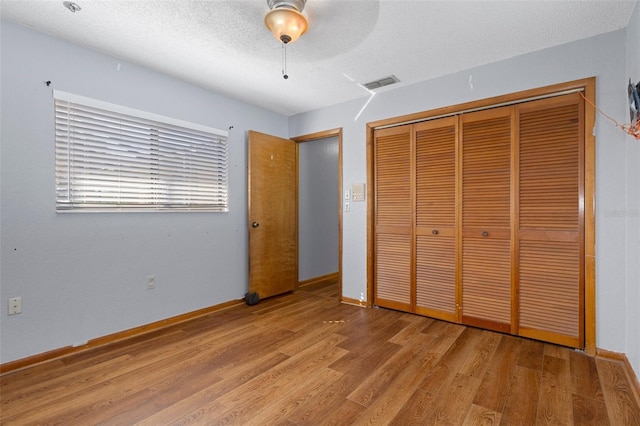 unfurnished bedroom with ceiling fan, a closet, a textured ceiling, and light wood-type flooring