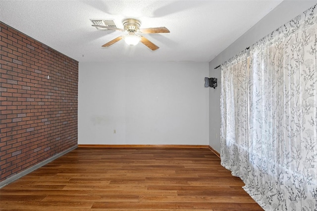 empty room featuring a textured ceiling, hardwood / wood-style flooring, ceiling fan, and brick wall