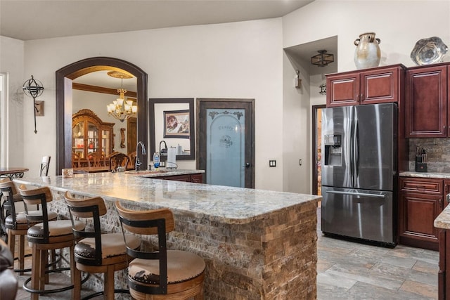 14101 Andrew Scott Rd, Spring Hill, FL 34609 - kitchen with stainless steel fridge with ice dispenser, light stone counters, a kitchen breakfast bar, arched walkways, and reddish brown cabinets