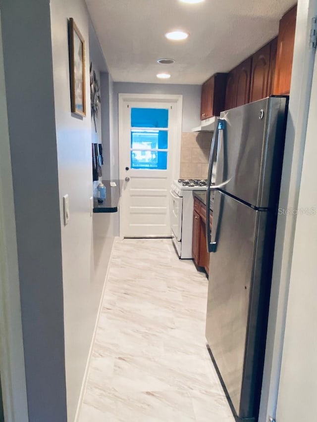 kitchen featuring decorative backsplash, white gas range, and stainless steel refrigerator