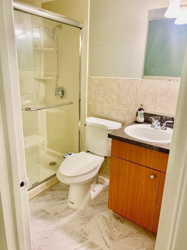 bathroom with a shower with door, vanity, tile walls, and toilet