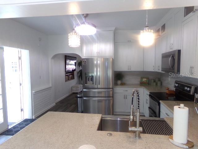 kitchen with white cabinetry, hanging light fixtures, appliances with stainless steel finishes, decorative backsplash, and dark wood-style floors