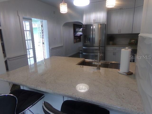 kitchen featuring arched walkways, stainless steel fridge with ice dispenser, a breakfast bar, a peninsula, and white cabinetry