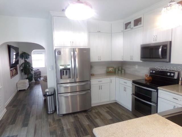 kitchen featuring arched walkways, light countertops, appliances with stainless steel finishes, and dark wood-style floors