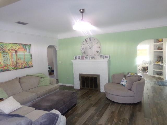 living area with arched walkways, a fireplace, and wood finished floors