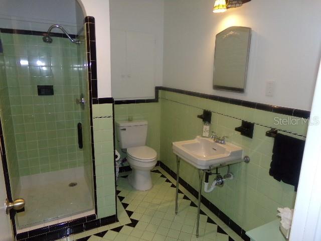 full bath with a wainscoted wall, tile walls, toilet, a stall shower, and a sink