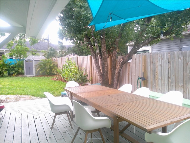 deck featuring a lawn, a fenced backyard, a storage unit, an outdoor structure, and outdoor dining space