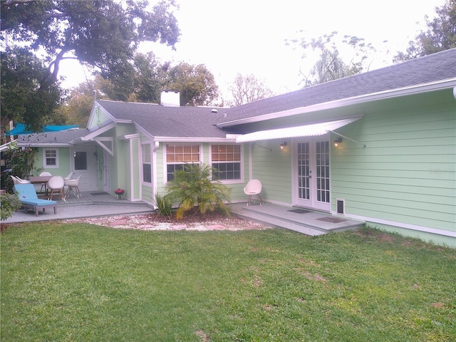 back of house with a patio, a yard, french doors, roof with shingles, and a chimney