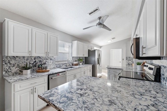 kitchen featuring lofted ceiling, ceiling fan, light stone countertops, appliances with stainless steel finishes, and white cabinetry