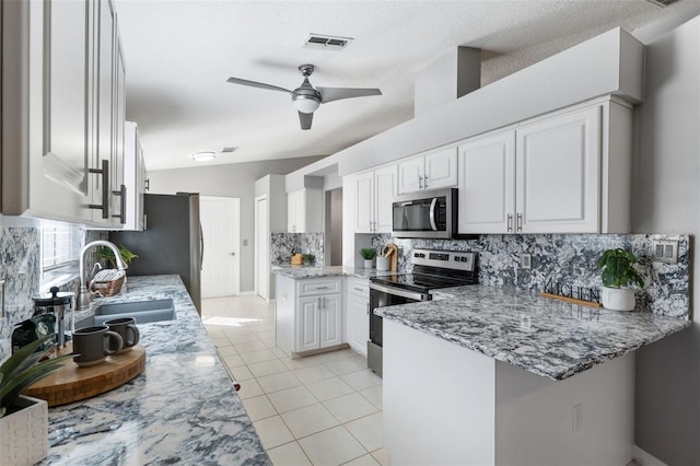 kitchen with kitchen peninsula, light stone countertops, stainless steel appliances, sink, and white cabinets