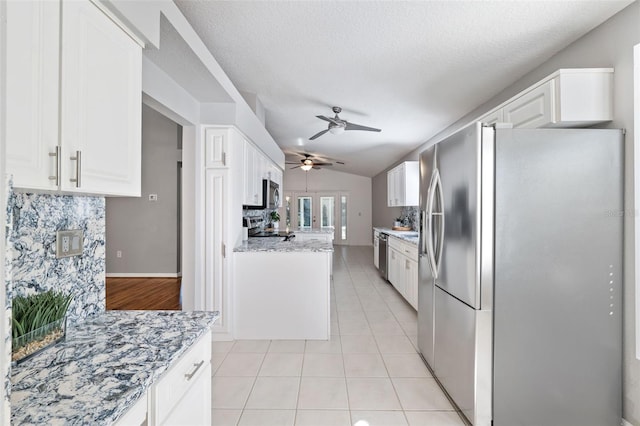 kitchen with lofted ceiling, white cabinets, light tile patterned floors, appliances with stainless steel finishes, and tasteful backsplash