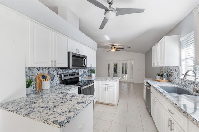 kitchen with white cabinets, appliances with stainless steel finishes, vaulted ceiling, and light stone countertops