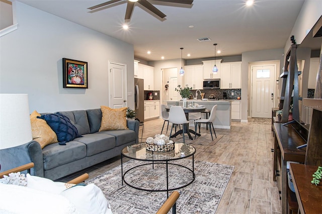 living room with light wood-type flooring, ceiling fan, a barn door, and sink