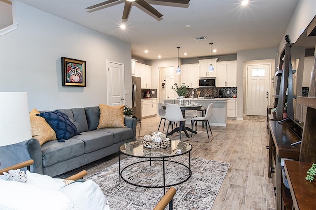 living room featuring ceiling fan, a barn door, light wood-type flooring, and sink