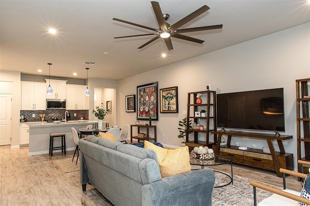 living room with light hardwood / wood-style flooring, ceiling fan, and sink