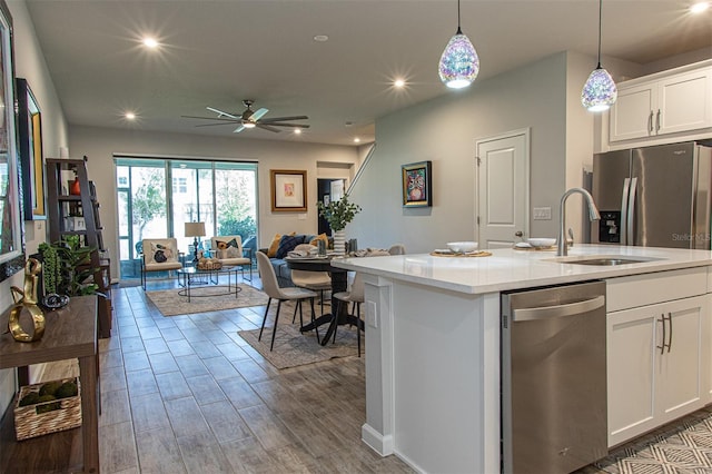 kitchen with ceiling fan, hanging light fixtures, a kitchen island with sink, white cabinets, and appliances with stainless steel finishes