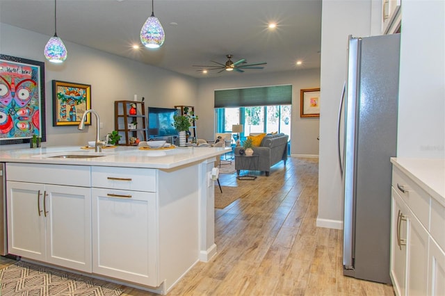 kitchen featuring ceiling fan, sink, hanging light fixtures, stainless steel fridge, and white cabinets