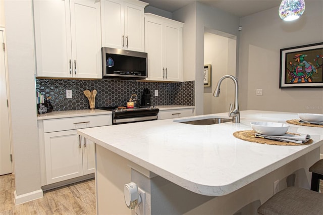 kitchen featuring sink, appliances with stainless steel finishes, a center island with sink, white cabinets, and light wood-type flooring