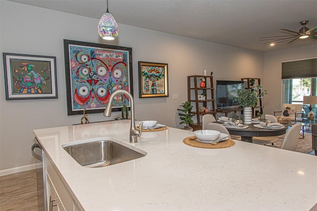 kitchen featuring ceiling fan, sink, hanging light fixtures, light stone counters, and an island with sink