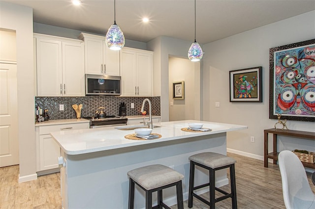 kitchen featuring white cabinetry, sink, stainless steel appliances, an island with sink, and decorative light fixtures