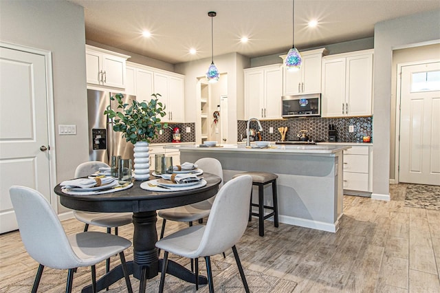 kitchen featuring pendant lighting, a kitchen island with sink, light wood-type flooring, white cabinetry, and stainless steel appliances