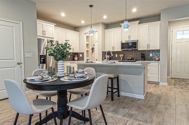 kitchen with a kitchen island with sink, decorative light fixtures, light hardwood / wood-style floors, white cabinetry, and stainless steel appliances