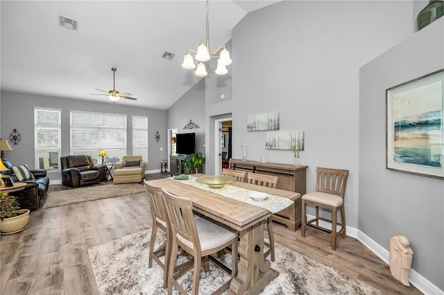 dining space with ceiling fan with notable chandelier, vaulted ceiling, and light hardwood / wood-style flooring