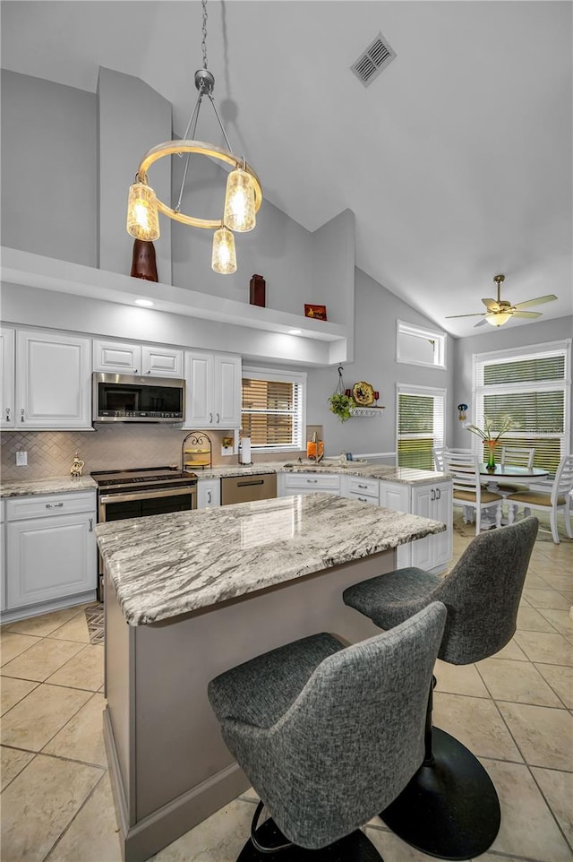 kitchen with white cabinetry, high vaulted ceiling, stainless steel appliances, and hanging light fixtures