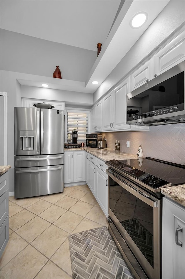 kitchen with appliances with stainless steel finishes, tasteful backsplash, white cabinetry, light tile patterned floors, and light stone counters