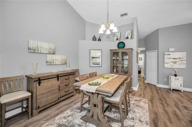 dining space with wood-type flooring, high vaulted ceiling, and a notable chandelier