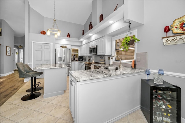 kitchen with appliances with stainless steel finishes, white cabinetry, beverage cooler, a kitchen breakfast bar, and kitchen peninsula