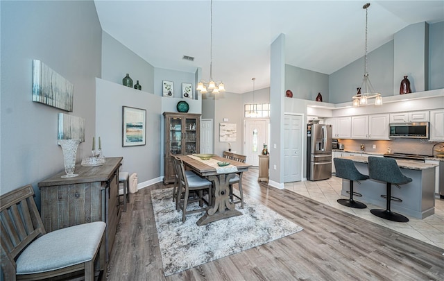 dining space featuring high vaulted ceiling, an inviting chandelier, and light hardwood / wood-style floors