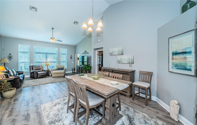 dining area with ceiling fan with notable chandelier, high vaulted ceiling, and light hardwood / wood-style flooring