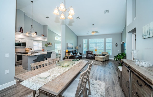 dining area with ceiling fan with notable chandelier, high vaulted ceiling, and light hardwood / wood-style flooring